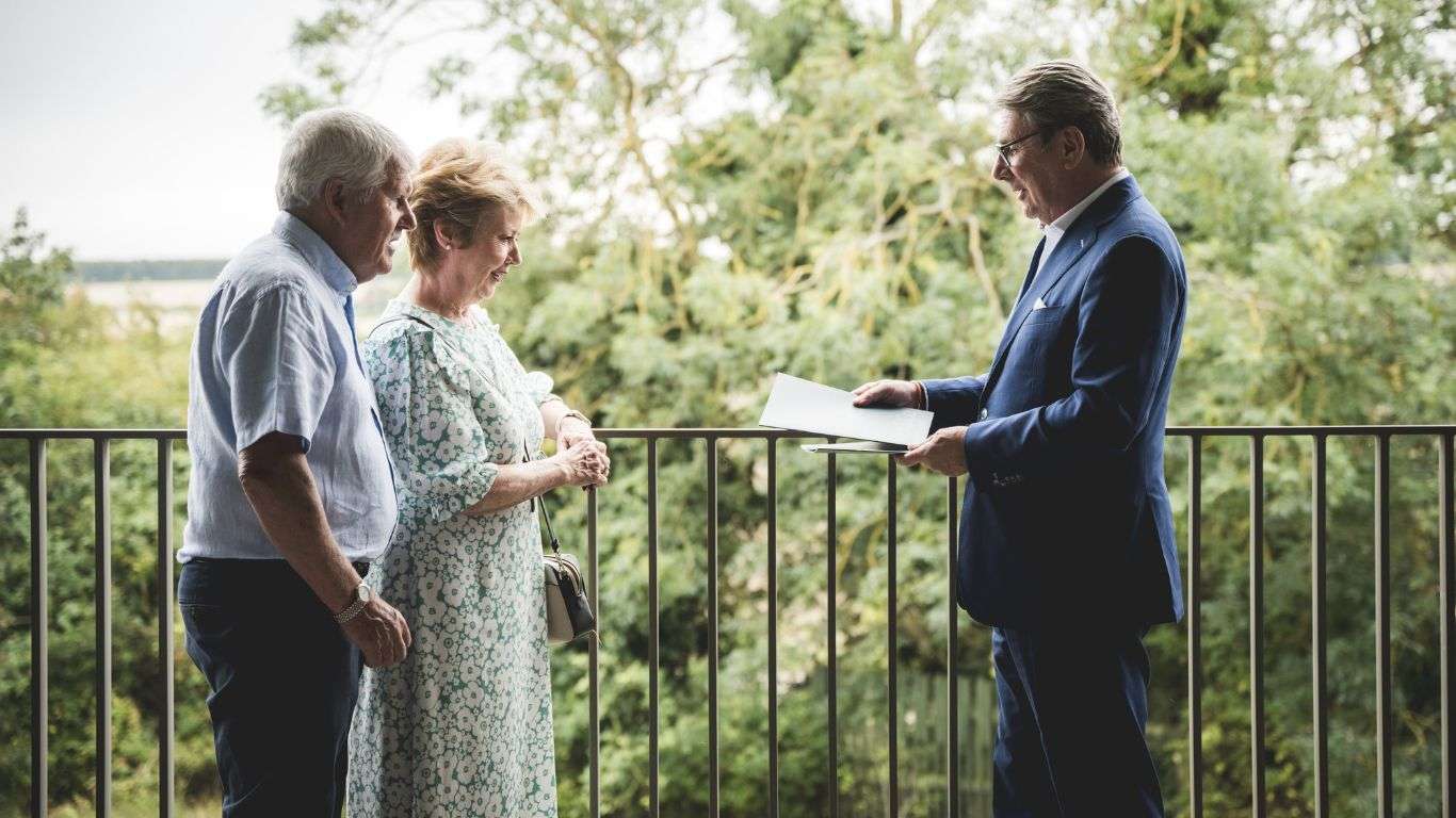 A man handing some paperwork to an elderly couple, by a railing