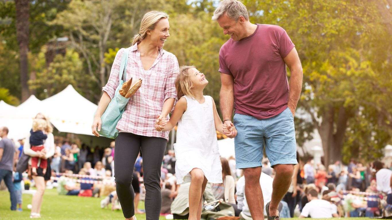 A young girl holding hands with a man and a woman, all smiling, as they attend a fete or festival