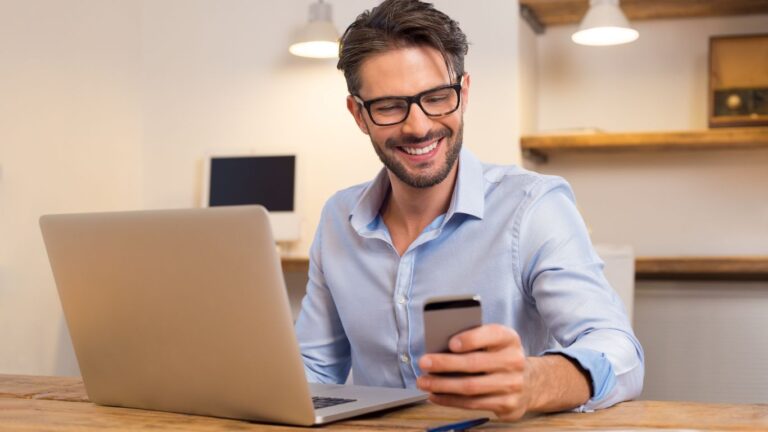 Man looking at phone infront of laptop thinking about Managing a Lettings Portfolio in Cambridge
