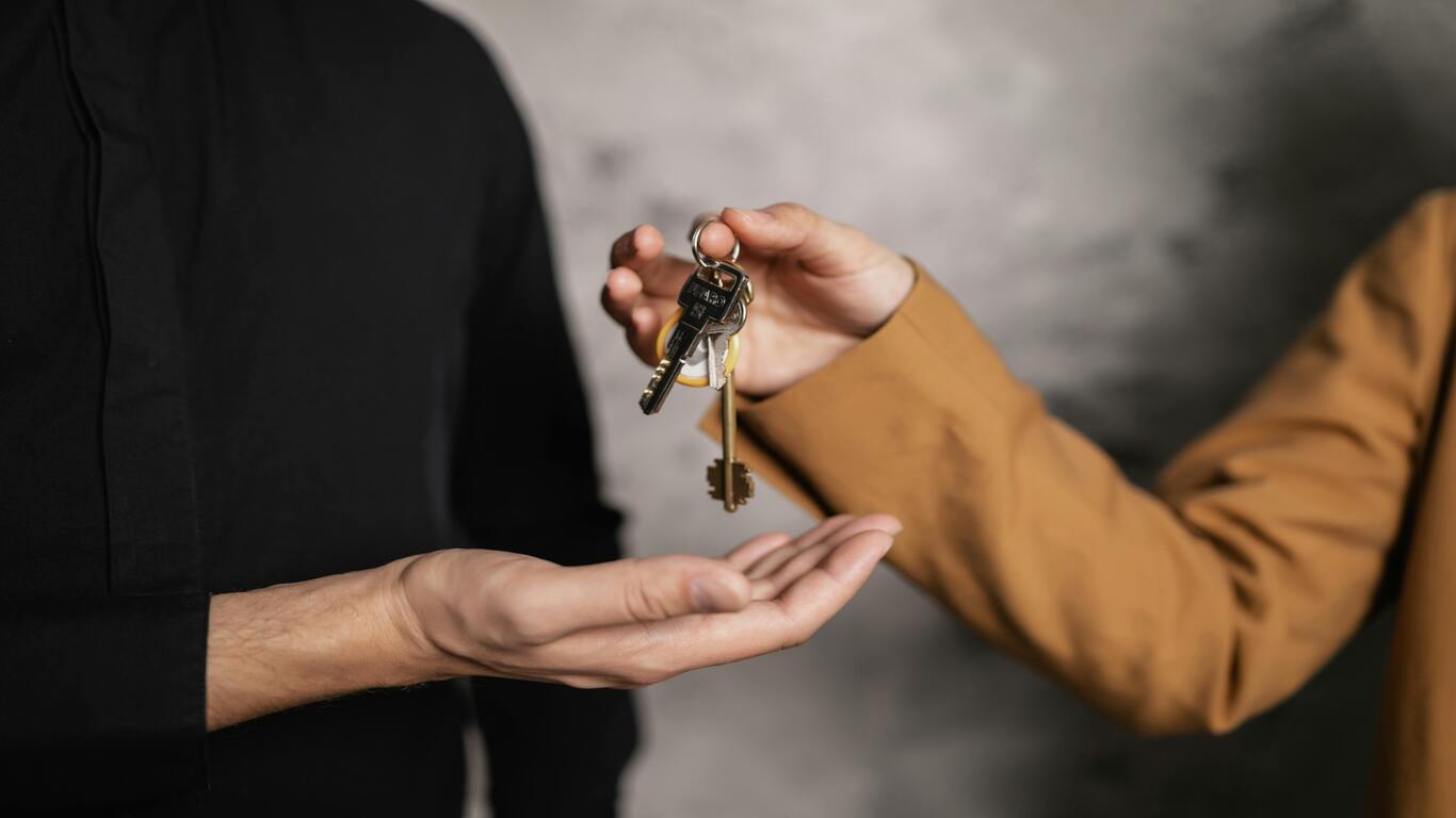 A person dropping keys into the hands of a person wearing black in a grey room