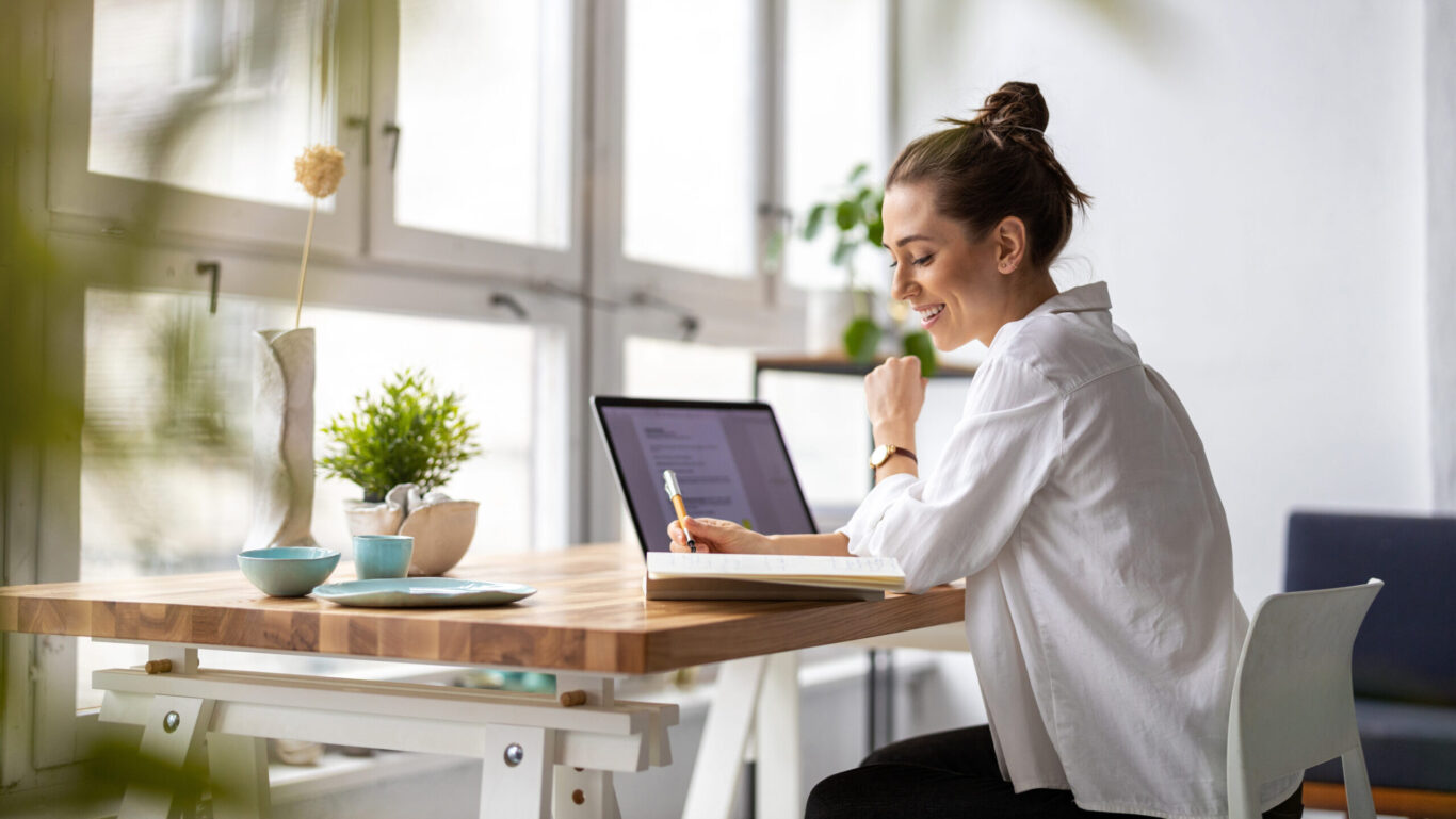 A woman smiling while she works at a desk in a home office