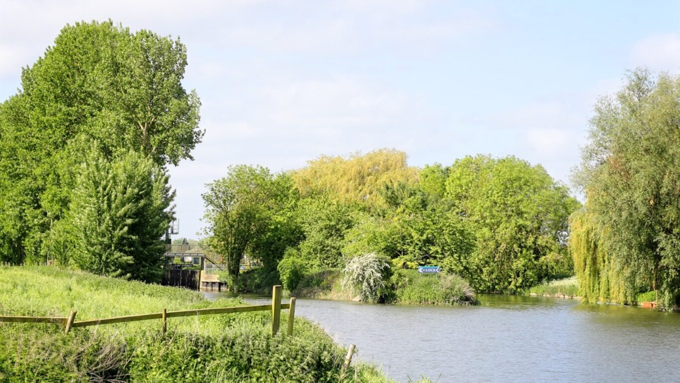 A river running through a green field, partially bordered by a fence